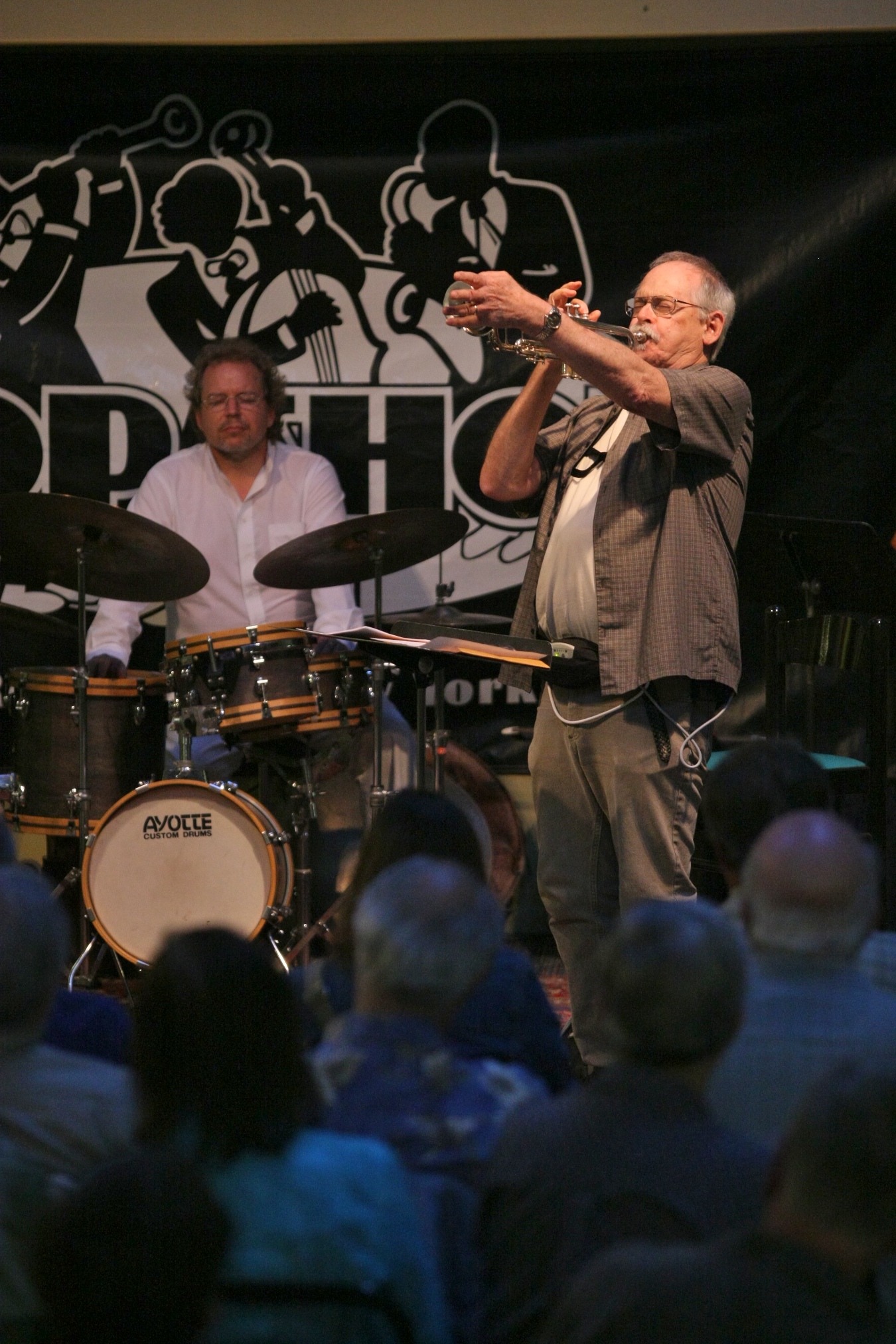 Paul Smoker playing trumpet, with his hand over the bell, possibly holding a mute, with Phil Haynes playing drums, during a concert